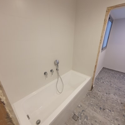 אמבטיה לבנה עם ברזים וקיר אריחים לבן