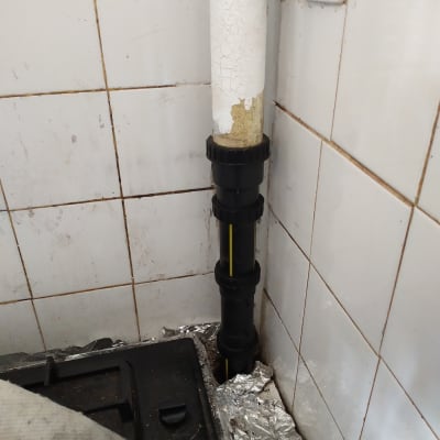 צינור פלסטיק שחור עם חיבורים ליד קיר אריחים