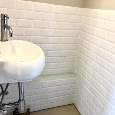 כיור לבן עם ברז מתכת על קיר אריחים לבנים