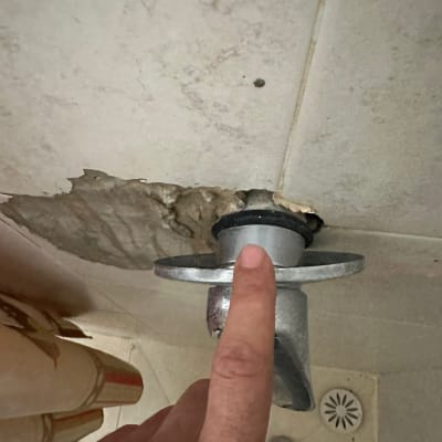 אצבע מצביעה על נזילה בתקרה ליד צינור מתכת
