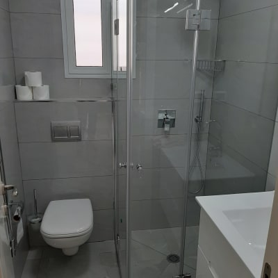 חדר אמבטיה משופץ עם מקלחון זכוכית ואסלה תלויה