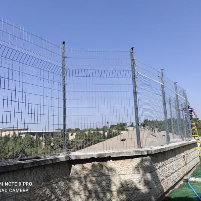 גדר מתכת גבוהה על קיר אבן עם אדם על סולם