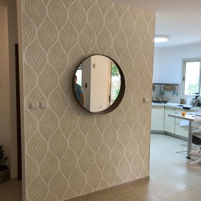 קיר עם טפט דוגמת עלים ומראה עגולה