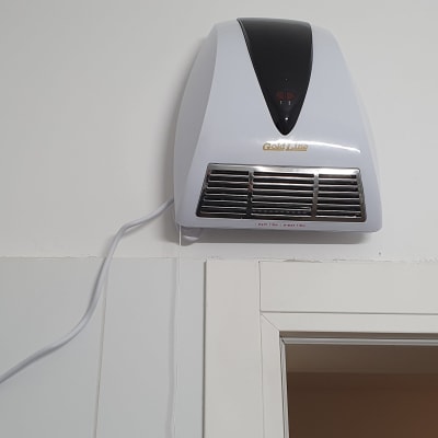 מאוורר חימום מותקן על קיר עם כבל חשמל מחובר לשקע