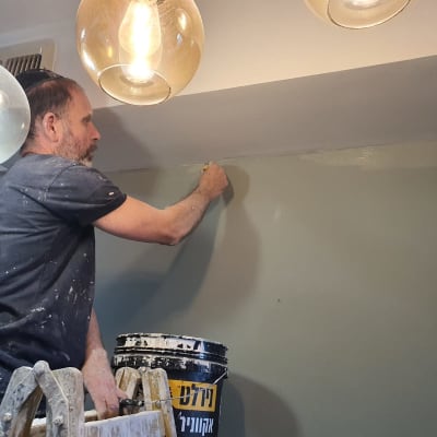 אדם צובע קיר עם מברשת ודלי צבע