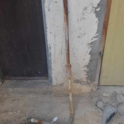 צינור חלוד עם חיבורים על רצפה ליד קיר