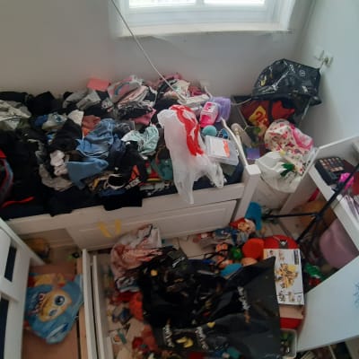 חדר מבולגן עם בגדים, צעצועים ושקיות על המיטה והרצפה.