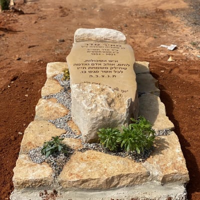 מצבה מאבן עם כיתוב בעברית וצמחים מסביב