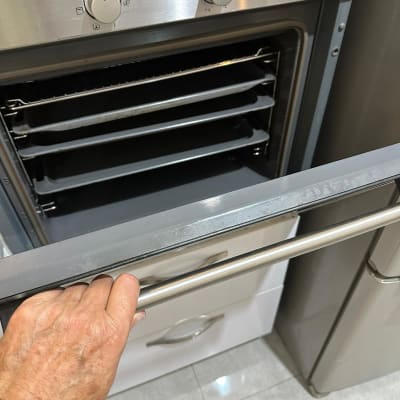 יד פותחת דלת תנור עם מגשים לניקוי