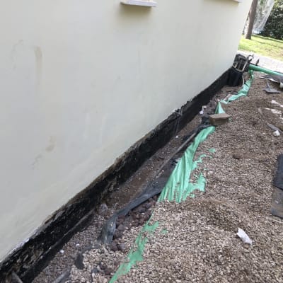 קיר עם איטום שחור, יריעות פלסטיק ואבנים קטנות