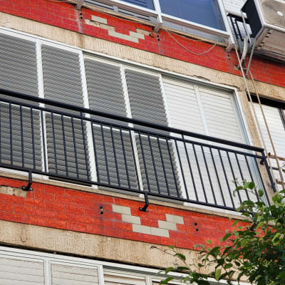 מעקה מתכת שחור מול חלונות עם תריסים אפורים