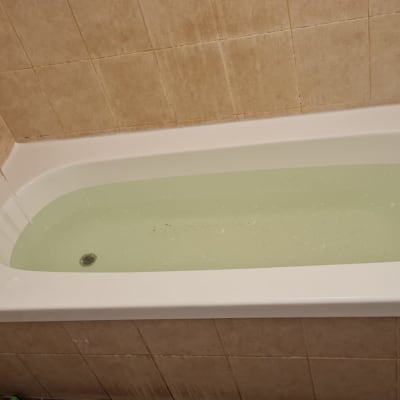 אמבטיה מלאה מים עם ברז פתוח על קיר אריחים