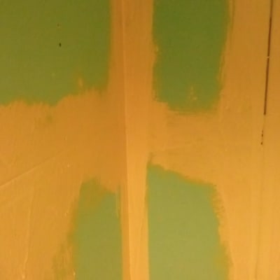 קיר צבוע חלקית בצבע כתום על רקע ירוק