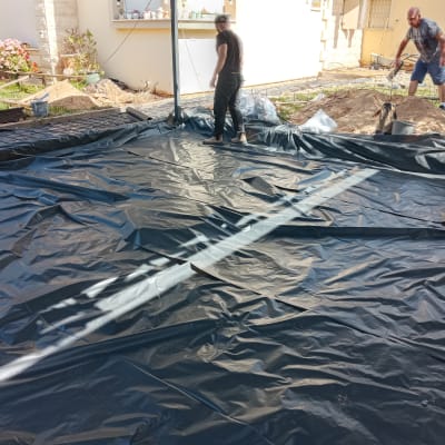 שני אנשים פורשים יריעת פלסטיק שחורה על הקרקע