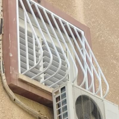 סורגי מתכת לבנים על חלון עם מזגן חיצוני