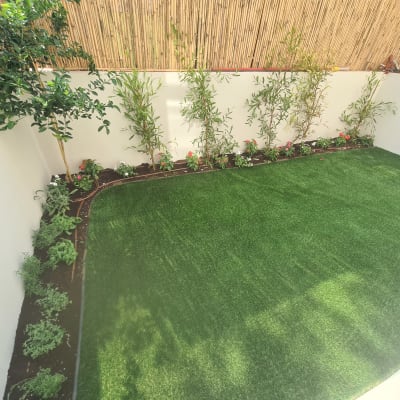 גינה עם דשא מלאכותי, צמחים ופרחים לאורך הקיר