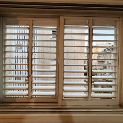 תריסים לבנים פתוחים בחלון עם נוף עירוני ברקע