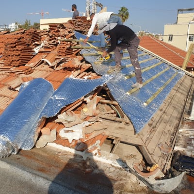 עובדים מתקינים בידוד על גג רעפים עם יריעות מבודדות.