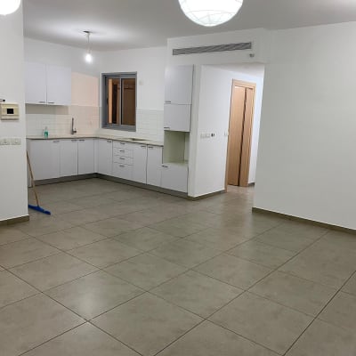 מטבח ריק עם ארונות לבנים ומטאטא בפינה