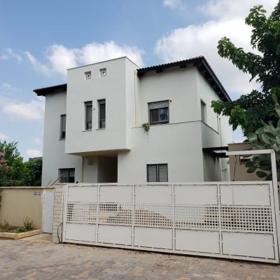 בית עם שער מתכת לבן ועצים מסביב