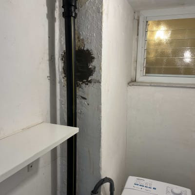 צינור שחור עם חיבורים ליד מכונת כביסה