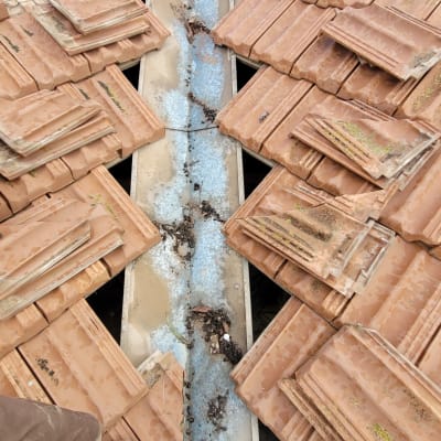 רעפים שבורים על גג עם תעלה מתכתית