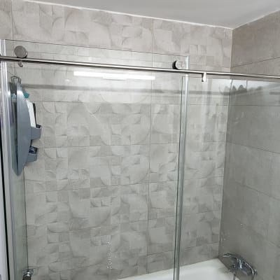 מקלחון זכוכית עם ברז מתכת וקיר אריחים אפור