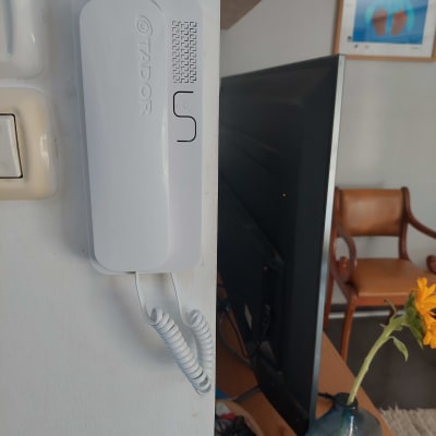 אינטרקום לבן מותקן על קיר עם כבל מסולסל