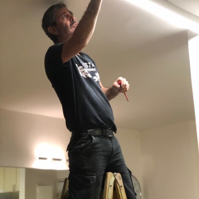 חשמלאי עומד על סולם ומתקן תאורה בתקרה