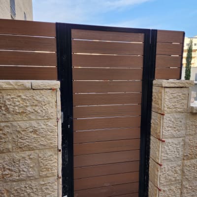 שער עץ חום במסגרת מתכת שחורה בין עמודי אבן