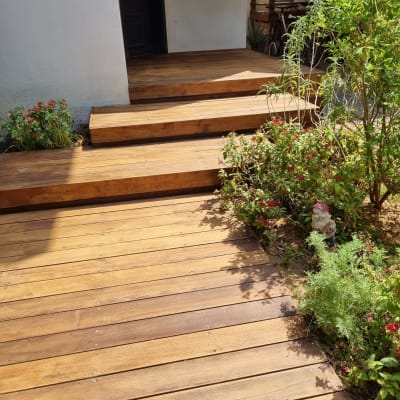 דק עץ עם מדרגות ליד צמחייה וכניסה לבית