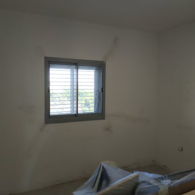 קיר לבן עם סימני תיקון, חלון וציוד מכוסה בניילון