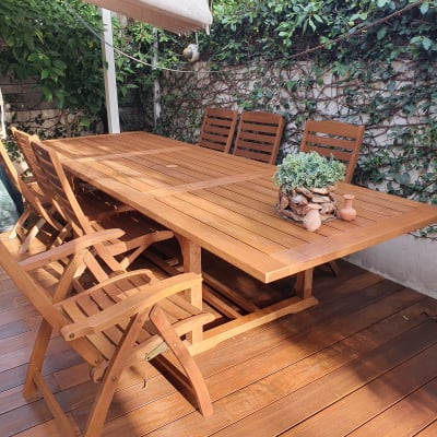 שולחן עץ עם כיסאות ועציץ על דק בגינה