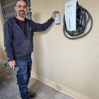 חשמלאי ליד מטען לרכב חשמלי עם מקדחה ביד