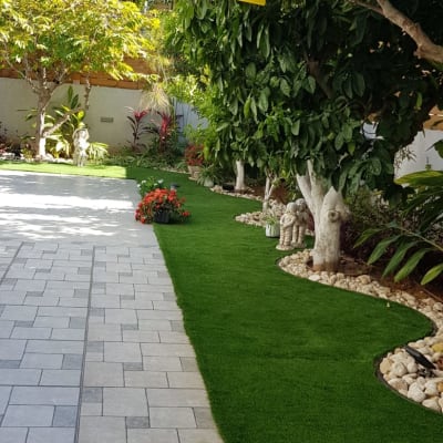 עצים עם דשא מלאכותי ופרחים בגינה מטופחת