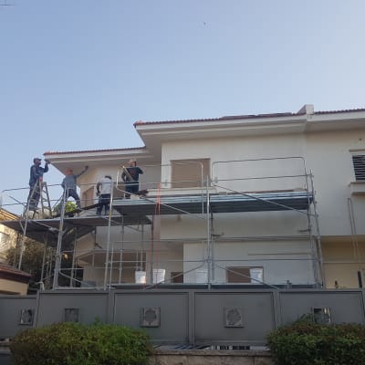 פועלים על פיגומים צובעים קיר חיצוני של בית