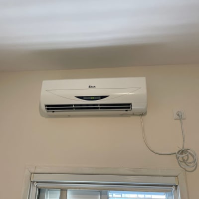 מזגן קיר לבן מותקן מעל חלון עם כבל חשמל