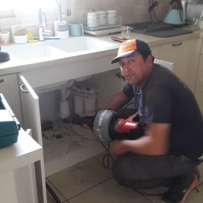 אינסטלטור עובד מתחת לכיור עם כלי עבודה חשמלי