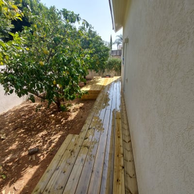 דק עץ ליד קיר בית עם עצי פרי