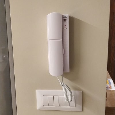 אינטרקום לבן מותקן על קיר עם כבל טלפון