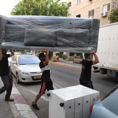 שלושה אנשים נושאים ספה עטופה בניילון ברחוב