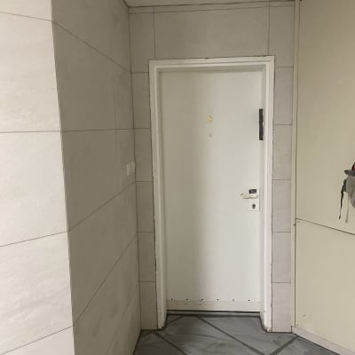 דלת לבנה עם קירות מרוצפים ורצפה עם סימני שיפוץ