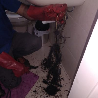 אינסטלטור עם כפפות אדומות מנקה סתימה בכיור