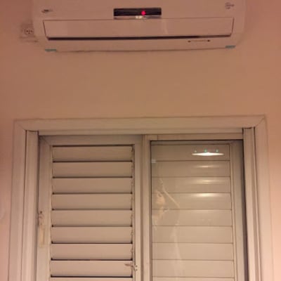 מזגן מותקן על קיר מעל חלון עם תריסים