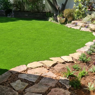 גינה עם דשא סינתטי, שביל אבנים וצמחים צעירים