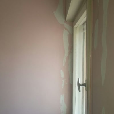 קיר ורוד עם קילופי צבע ליד חלון