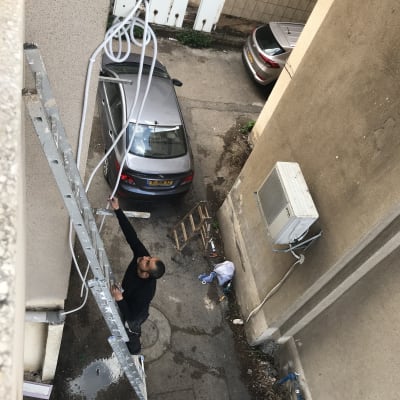 אדם על סולם מתקין צינורות למזגן על קיר חיצוני