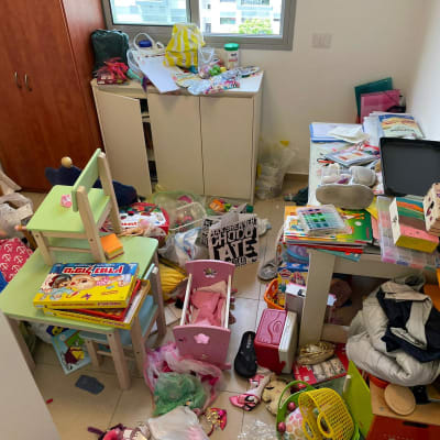 חדר מבולגן עם צעצועים, בגדים, שולחנות וכיסאות קטנים