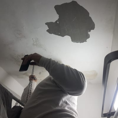 אדם בודק תקרה מתקלפת עם פנס ביד