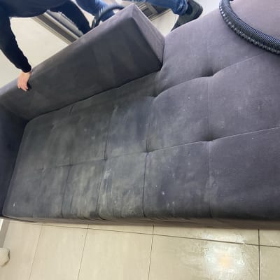 אדם מנקה ספה כהה עם שואב אבק